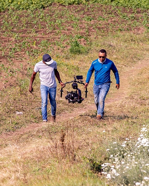 Two men in a field carrying camera equipment